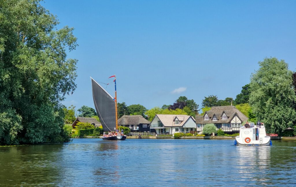 Wroxham and Hoveton, riverside houses with wherry boat and dayboat on Norfolk Broads near Wroxham